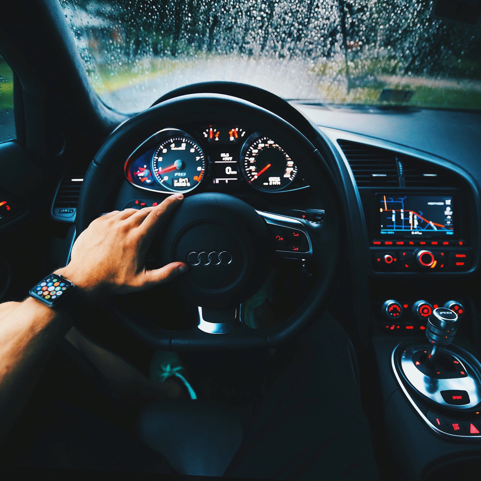 Audi R8 car interior and dashboard. The driver has his hand on the steering wheel.